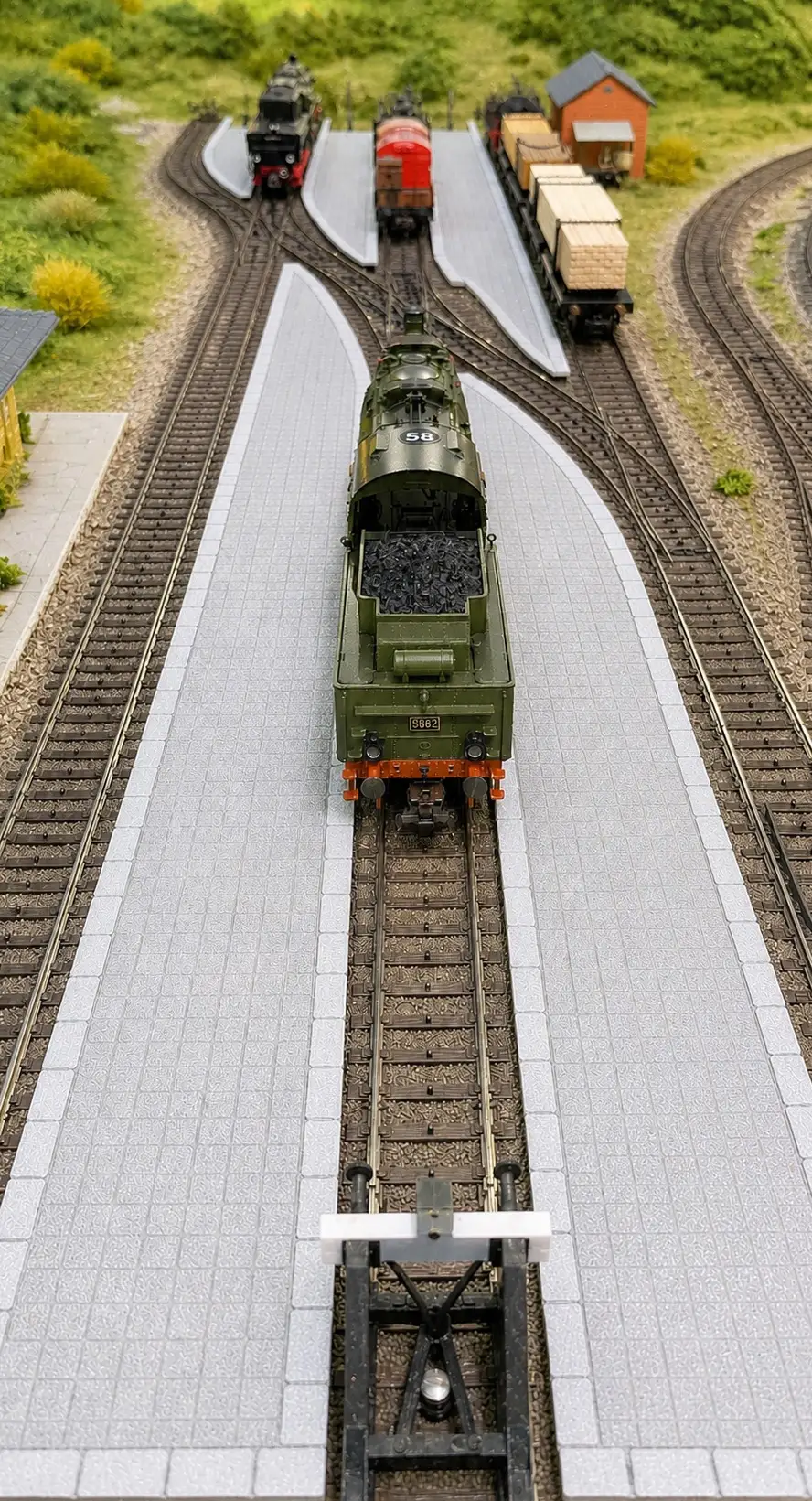 Modellbahnanlage in Spur H0 von oben: zwischen den Gleisen liegen mehrere helle Bahnsteige aus dem 3D-Druck, auf dem mittleren Gleis steht eine Dampflokomotive